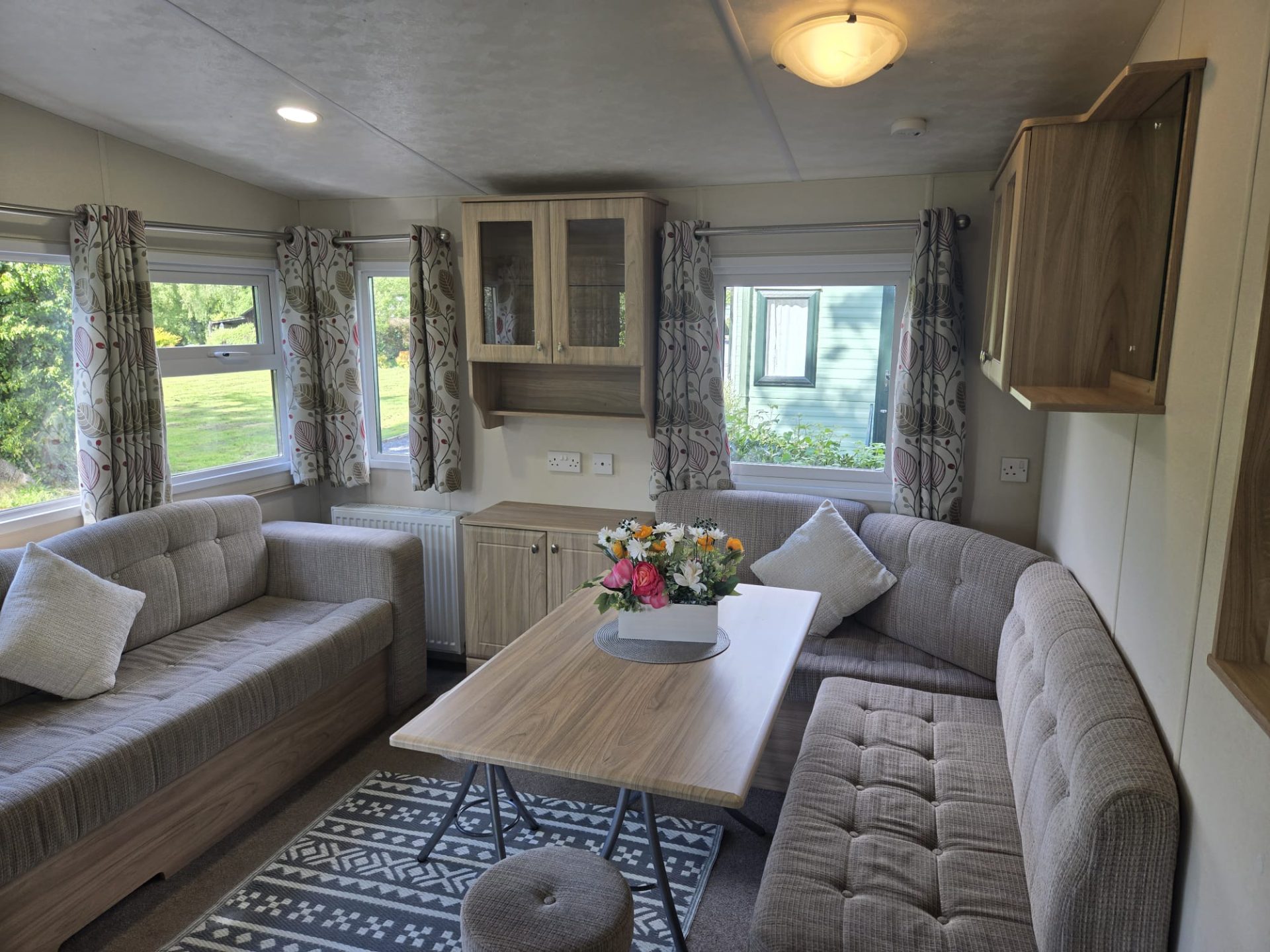 Interior lounge of a static caravan with grey sofas and countryside views through the windows